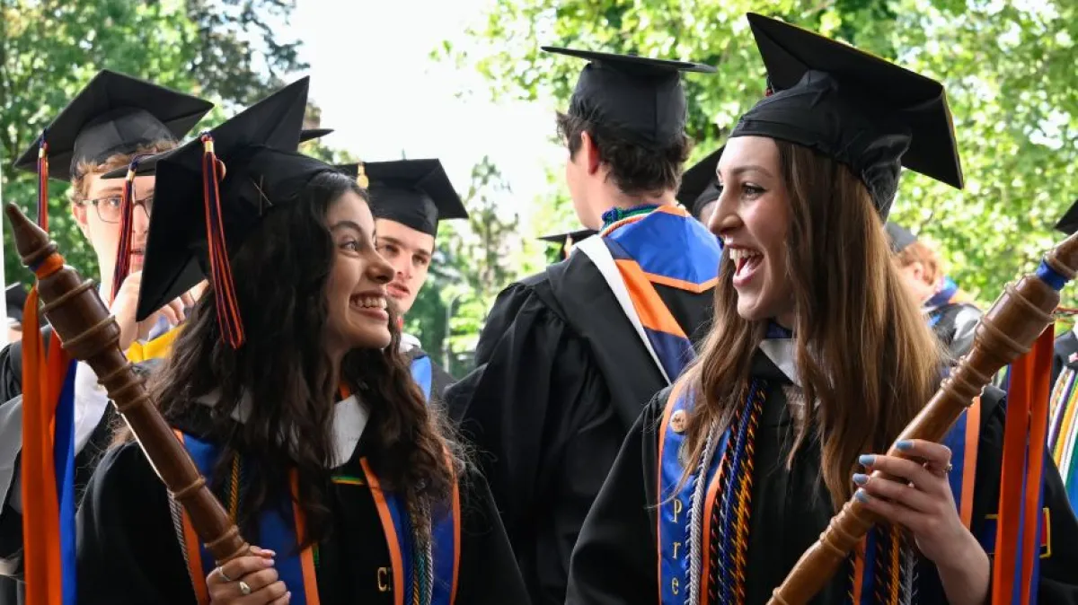 Graduates in caps and gowns celebrate outdoors with diplomas.