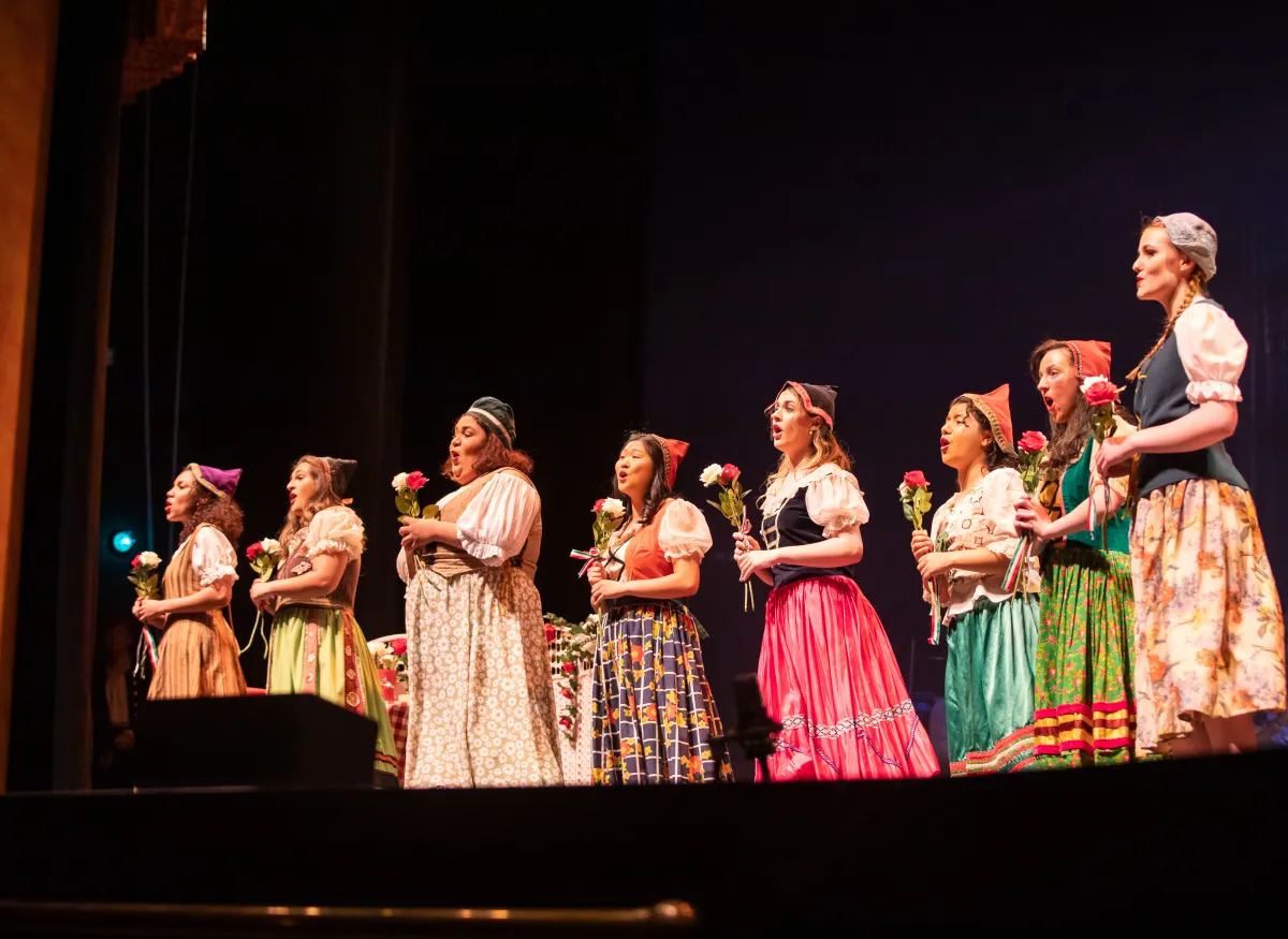A theatrical scene shows several performers onstage
