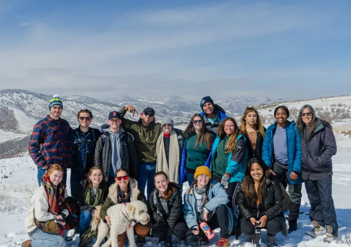 Group of people posing in a snowy mountain landscape with a dog in front