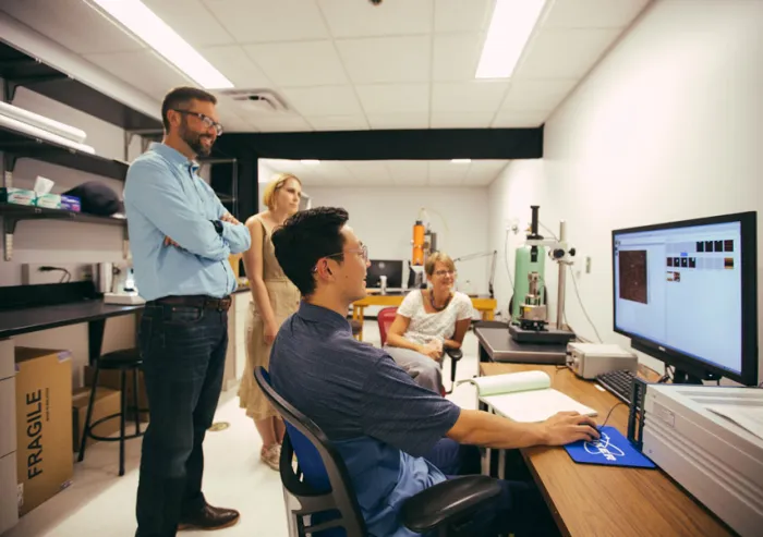 A student sitting at a computer shows his work to three other individuals.
