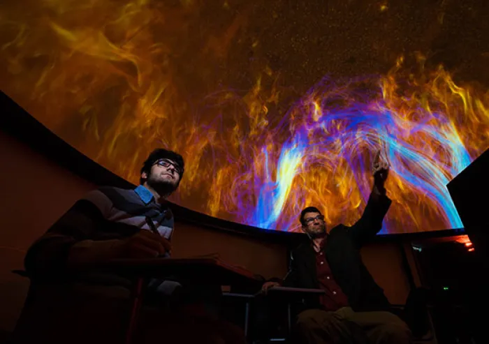 Student and Professor sit beneath a colorful planetarium display