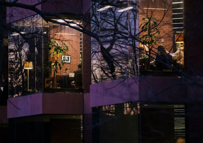 People work inside a glass-walled office at night.
