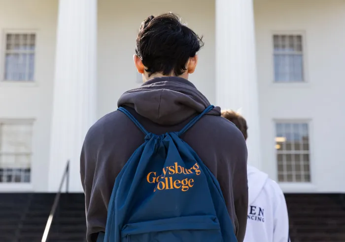 A student seen from behind walks toward the Penn Hall while wearing a dark backpack.
