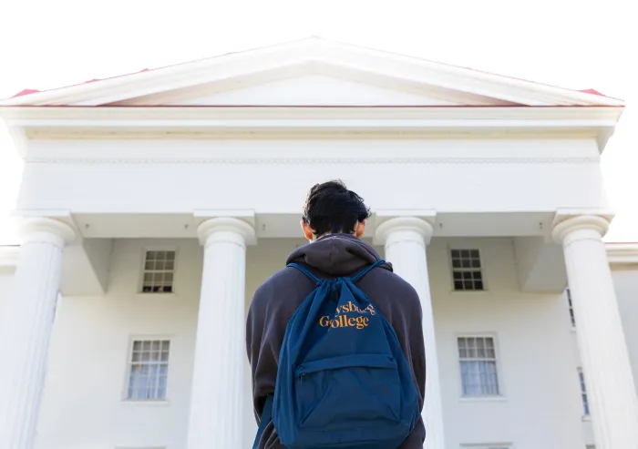 student with backpack looks up at white building with pillars