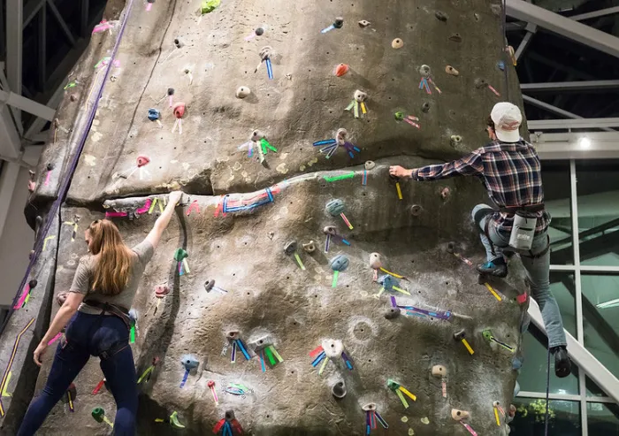 Two students climb on a climbing wall.