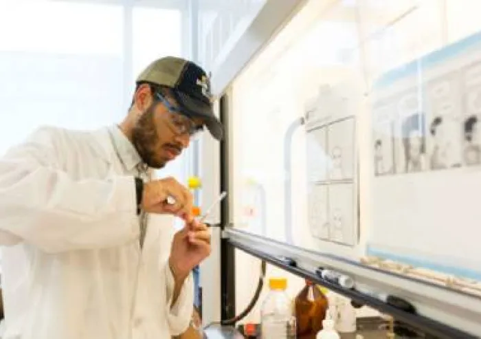 Student in a lab coat and safety glasses uses a pipette at a laboratory bench