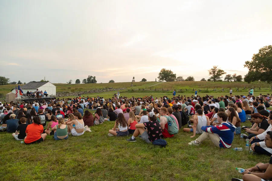 students sit in field with battlefields and podium in background
