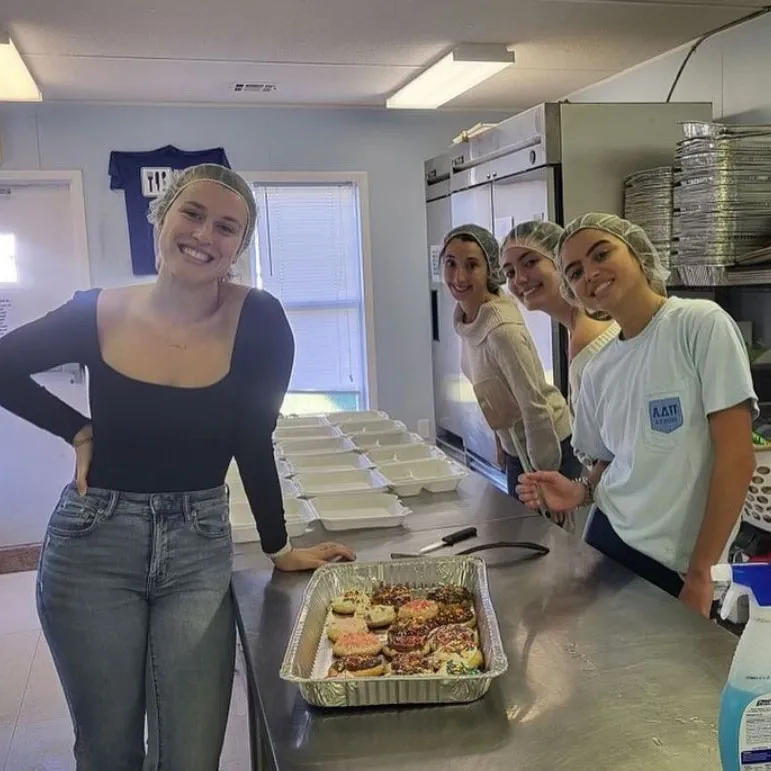 students in hairnets pose for camera with food containers on table