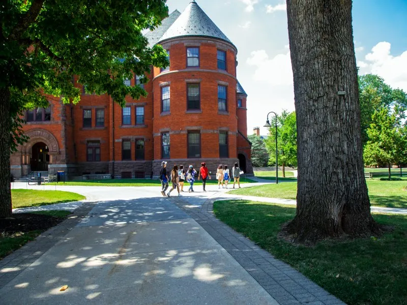 students walk on sidewalk in sunlight in front of brick building