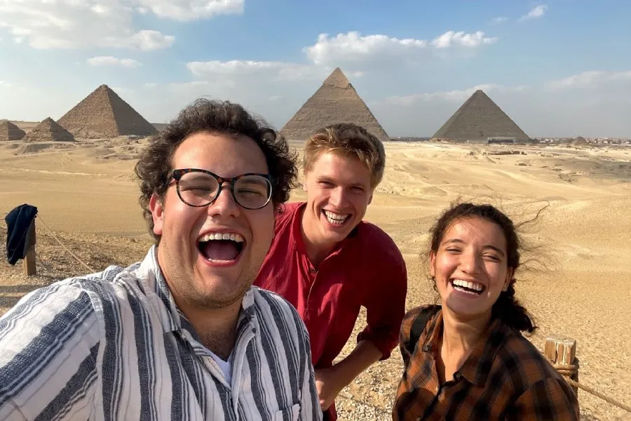 students smile for selfie in front of Egyptian pyramids