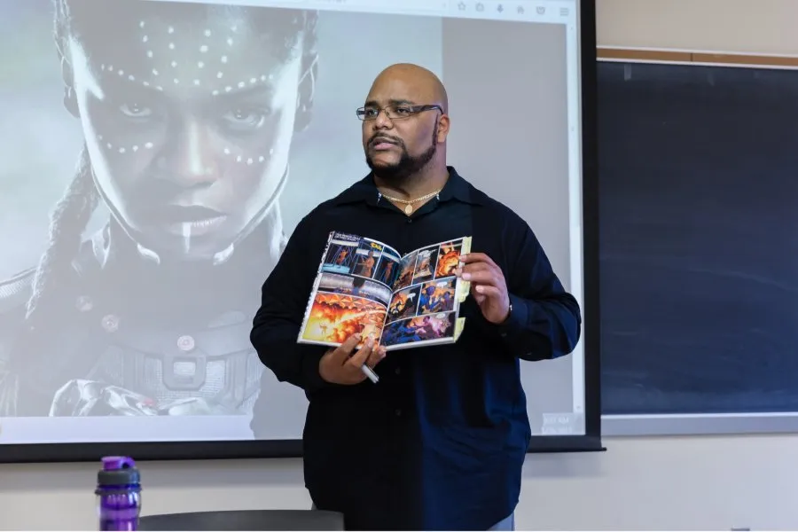 male alum holds up graphic novel with illustration on screen behind him