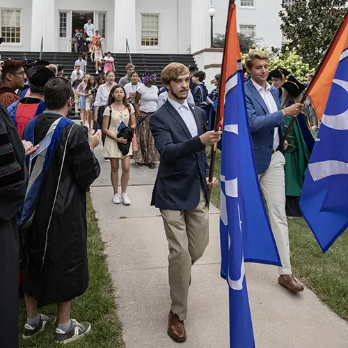 students process off of portico led by banner carriers