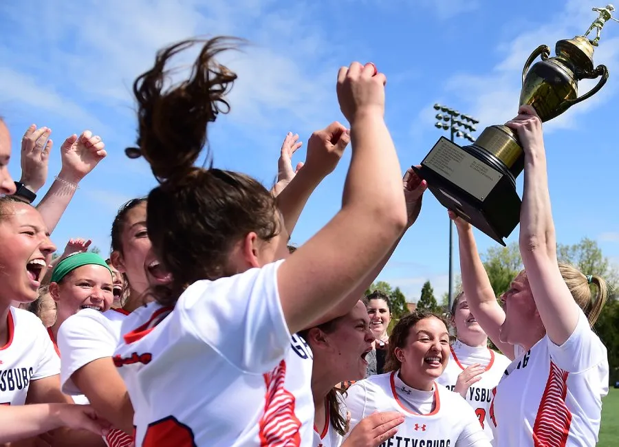 womens lacrosse team celebrates and holds trophy up