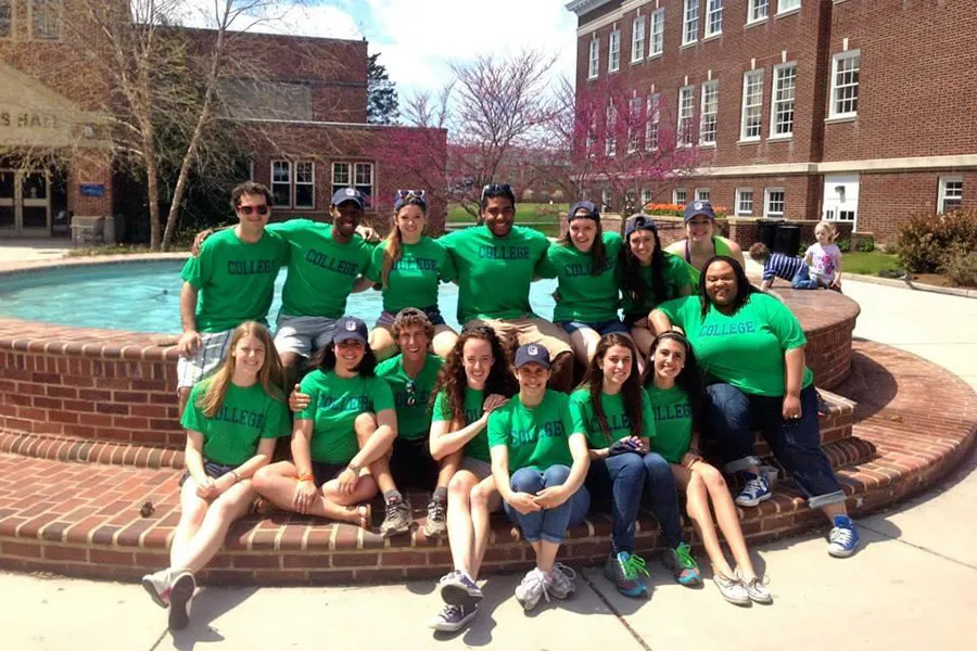 students pose in green shirts in front of campus fountain