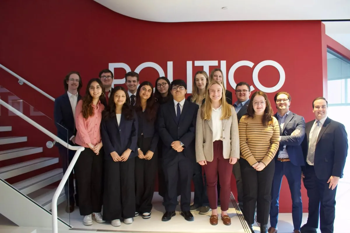 students in professional attire stand in front of Politico sign on wall