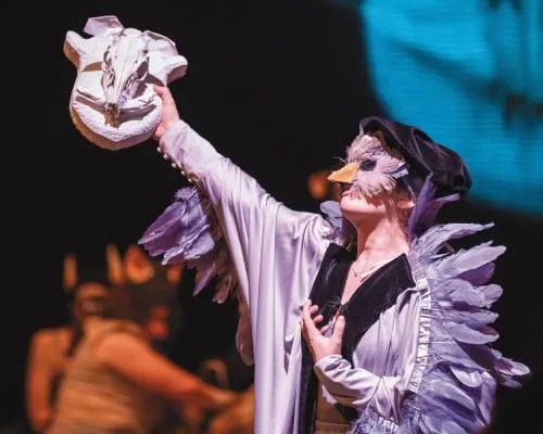 Costumed performer holds up a mask on stage.