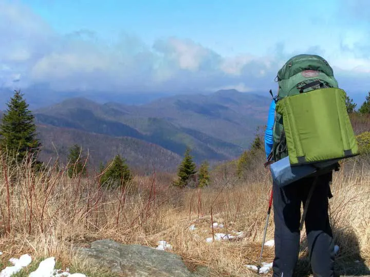Person hiking with a backpack in front of a mountain range.
