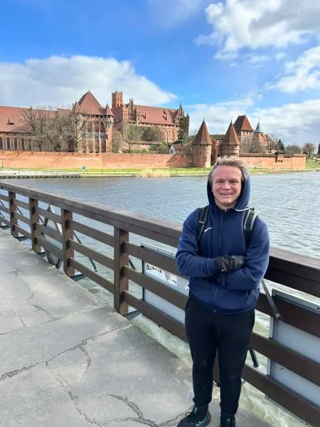 male student smiles on bridge in front of brick castle