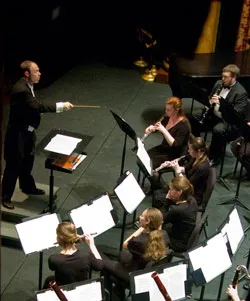 Conductor leads a seated chamber ensemble during a performance.