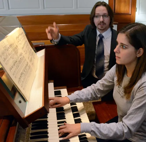 Student plays an organ while an instructor provides guidance.