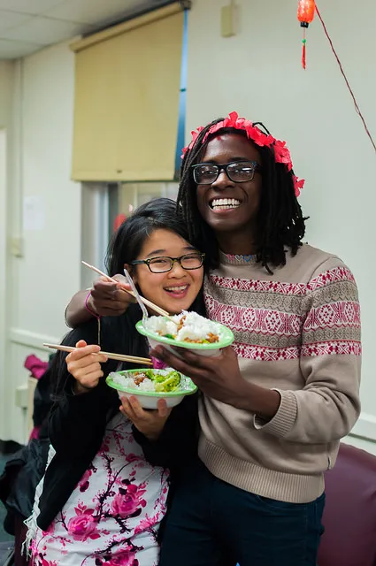 Two people smiling and holding bowls of food.