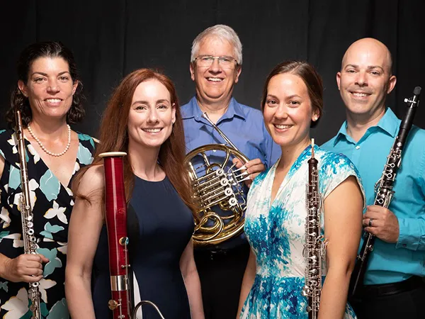 Musicians pose with their wind instruments, including an oboe, bassoon, French horn, and clarinet.