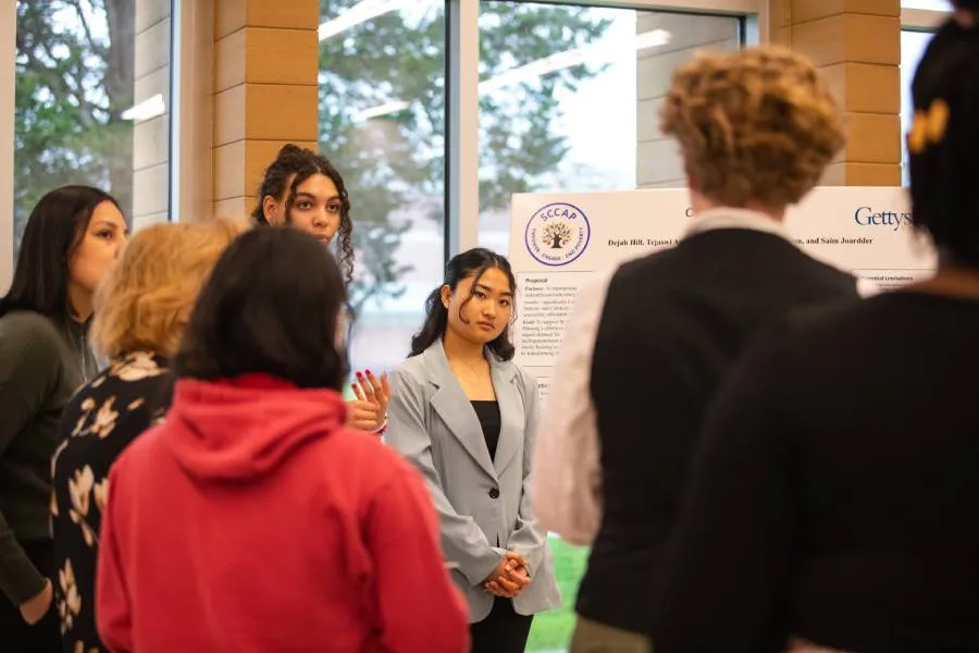 A student presents a project to attendees during an indoor campus showcase.