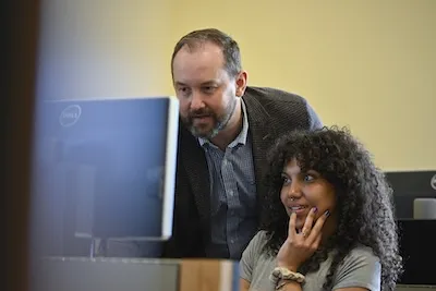 A student and professor work on a computer.
