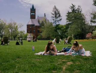 Two students doing homework while lying on the grass.