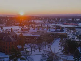 The sun sets over a snowy campus.