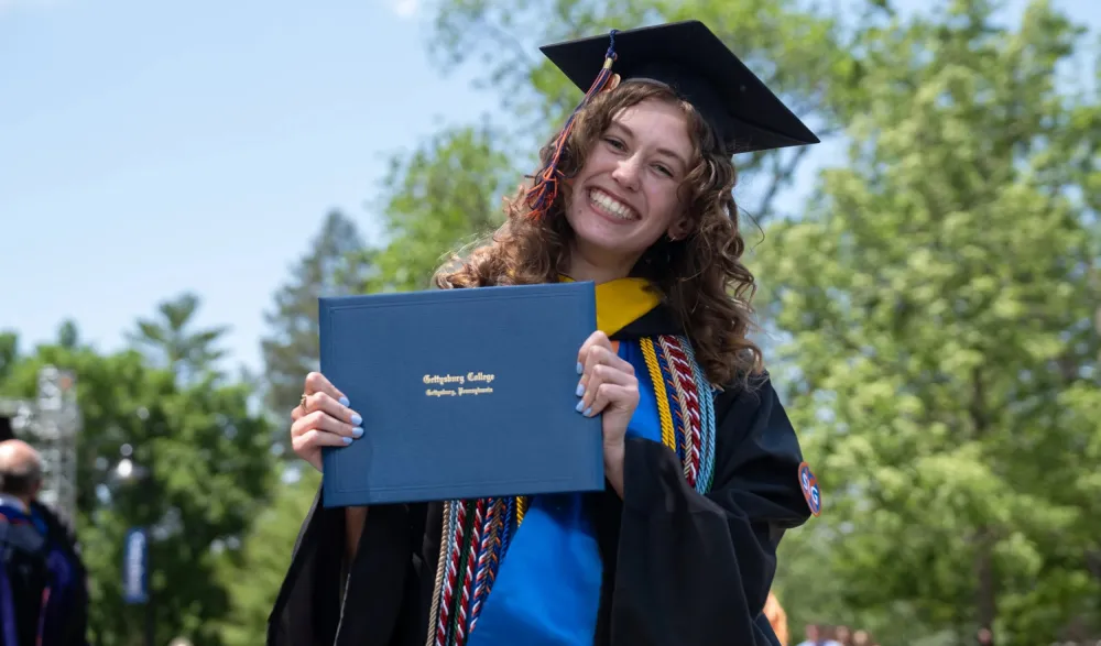 student smiles holding diploma at Commencment
