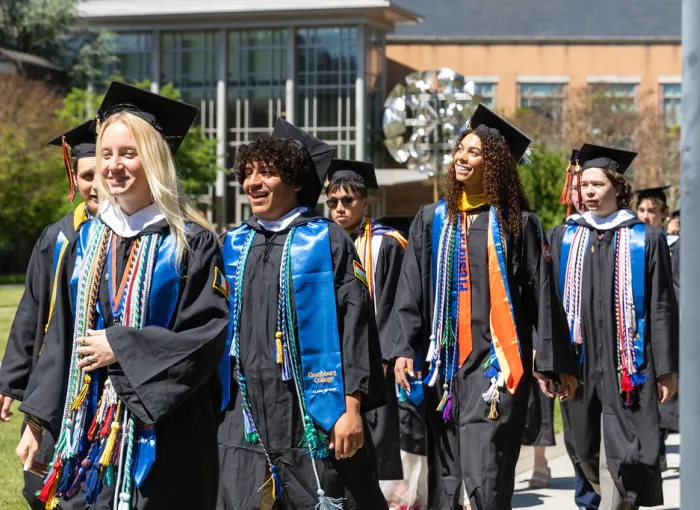 Graduates in colorful academic regalia pose outdoors.
