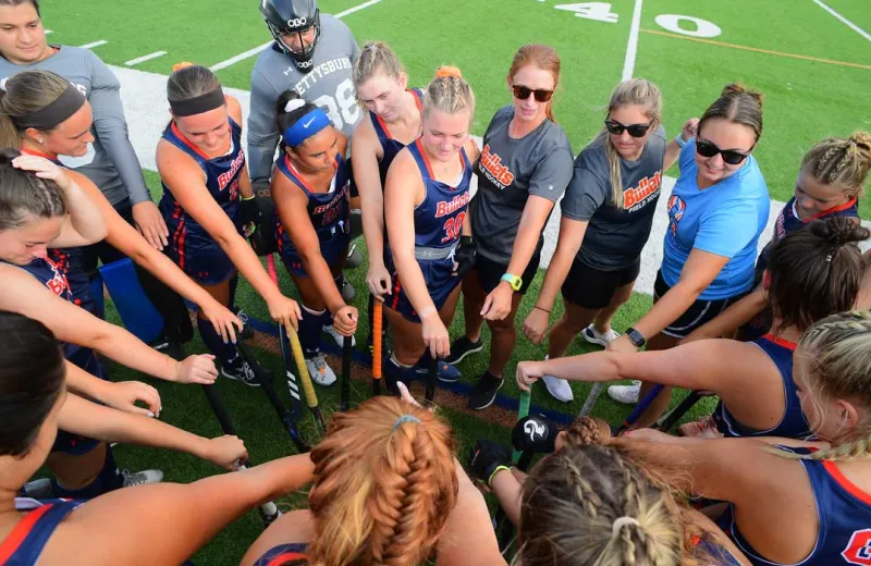 Lacrosse players gather in a team huddle on the turf.