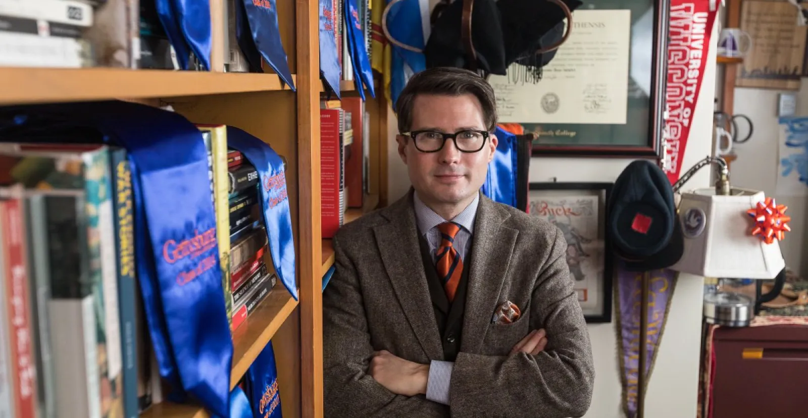 male prof poses leaning on bookcase