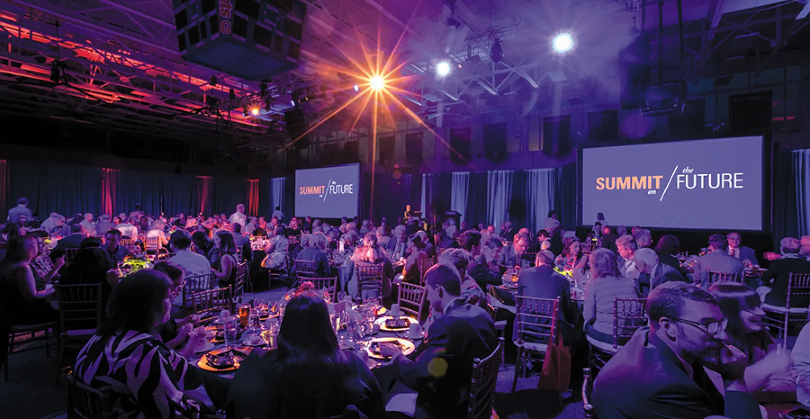 fancy dinner event in purple lighting with summit for the future on screen in background