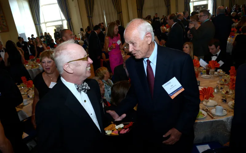 two male alumni speak with busy dinner event in background
