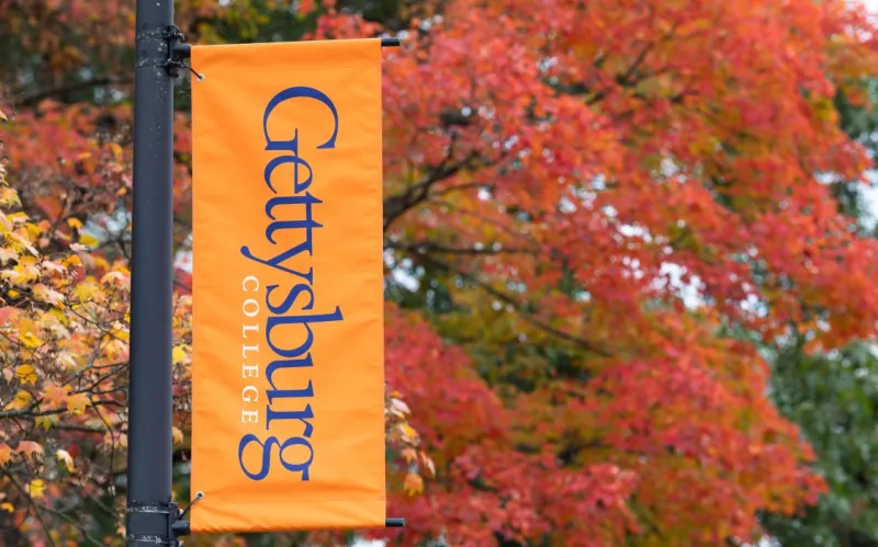 Gettysburg College lightpole banner with brilliant fall foliage in background