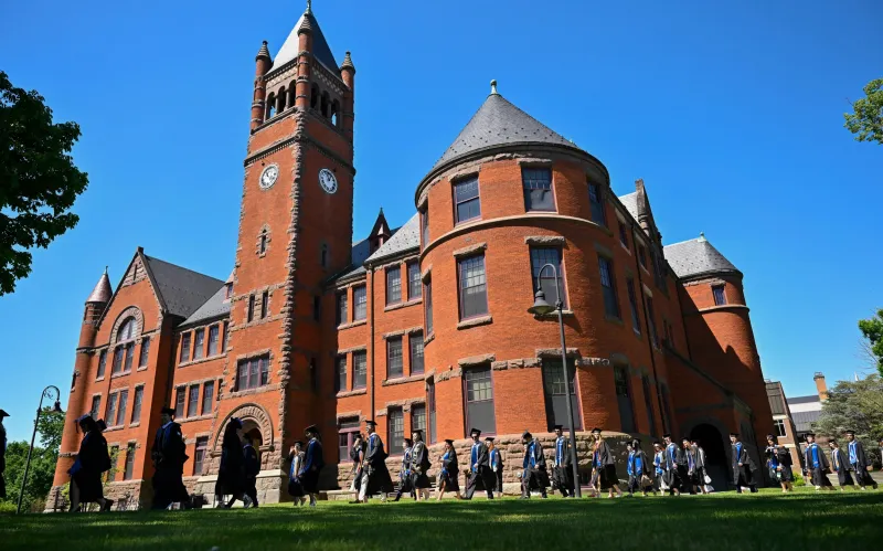 graduates process in front of large brick building