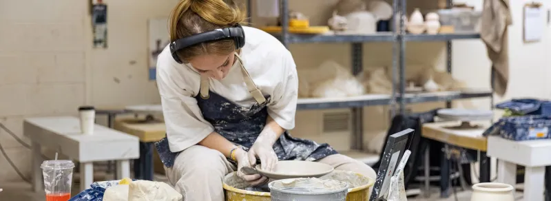 student throws pottery on wheel in ceramics studio